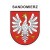 Naklejka z herbem Sandomierza i napisem Sandomierz nad herbem, herb i napis posiadają białą obwódkę, która jest białym tłem dla herbu Sandomierza i napisu. Wymiar naklejki 12 cm wysokości.