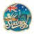 Naklejka Sydney z symbolami tego miasta, napisem Sydney i flagą Australii w tle. Naklejka jest wodoodporna, okrągła i kolorowa z kremową obwódką.